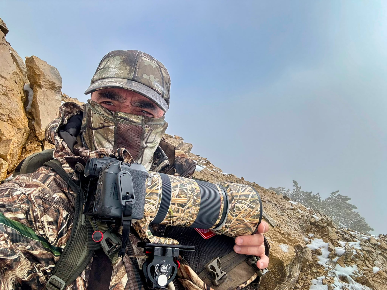 Patrick Fiori en affût, camouflé dans les rochers, téléobjectif à la main